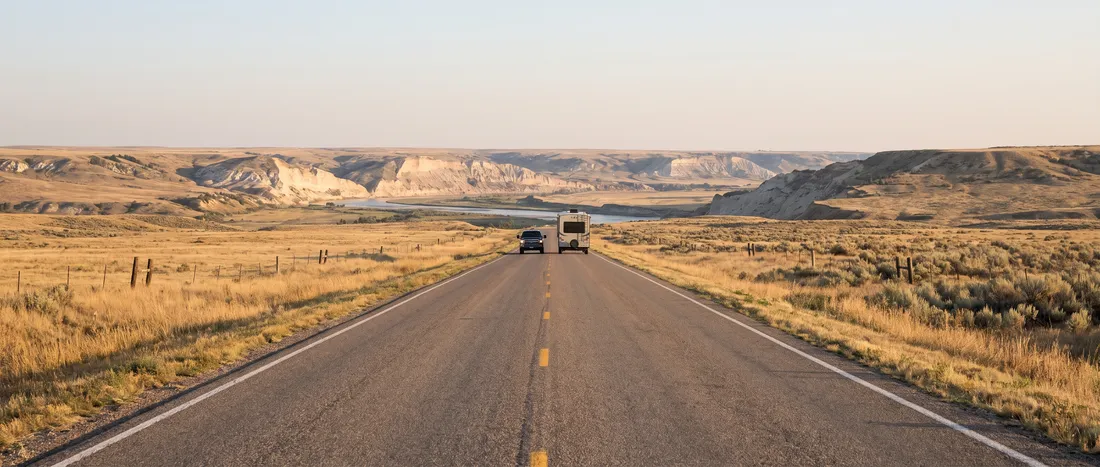 Two-lane prairie highway toward a river valley at sunrise